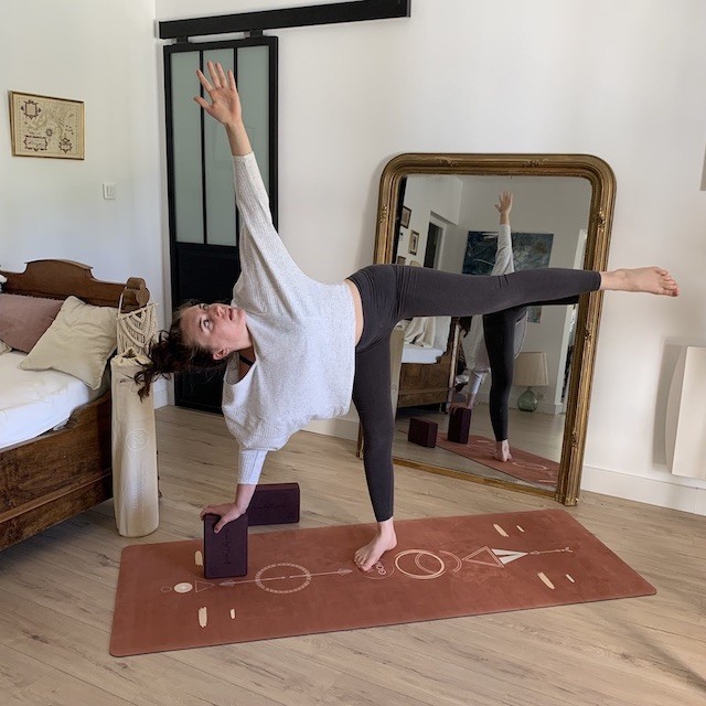 yogini réalise la posture du guerrier sur le côté en appui sur un bloc yogom