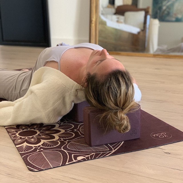jeune femme allongée sur un tapis de yoga yogom avec deux briques en eva bordeaux sous la tête