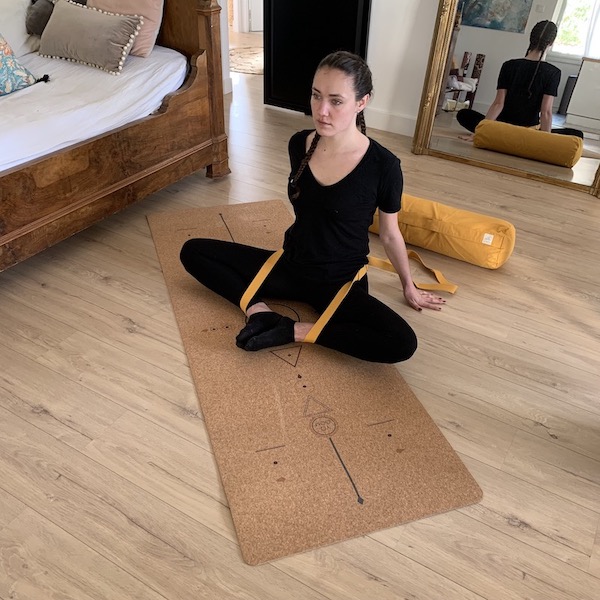 jeune femme en position du papillon avec une sangle de yoga jaune yogom sur un tapis de yoga en liège et caoutchouc recyclé yogom