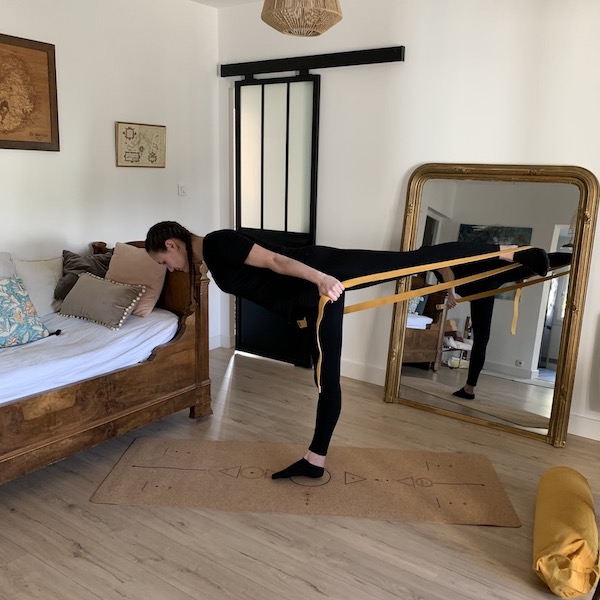 jeune femme en posture du guerrier avec sangle d'étirements et tapis en liège yogom