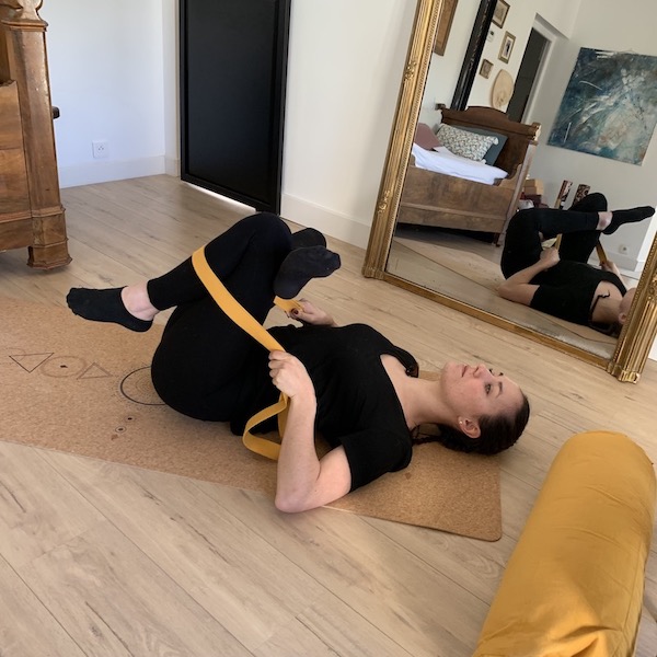 jeune femme sur le dos s'étire avec la sangle d'étirements yogom sur le tapis de yoga écologique yoogm