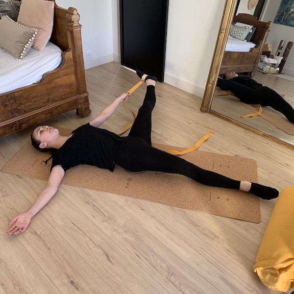 jeune femme s'étire la jambe gauche avec une sangle d'étirements yogom sur un tapis de yoga made in portugal