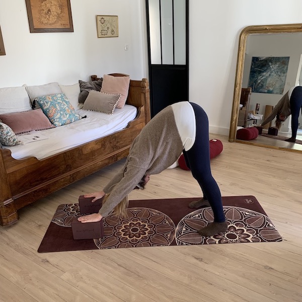 jeune femme en position chien tête en bas avec deux briques en mousse d'EVA recyclé sur un tapis en tpe et caoutchouc yogom